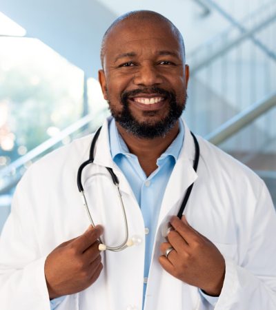 Vertical portrait of smiling african american male doctor in hospital corridor. Hospital, medical and healthcare services.